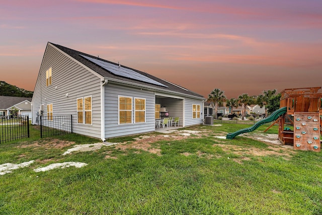 back of property with roof mounted solar panels, a lawn, a fenced backyard, and a playground
