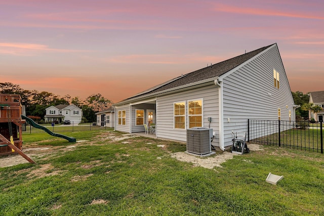 back of property at dusk featuring fence, a playground, a yard, and central AC unit