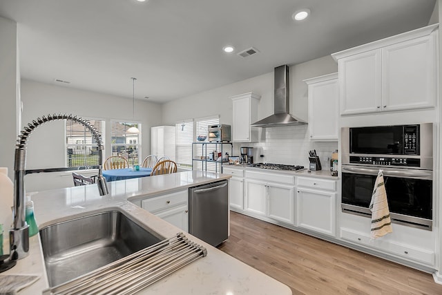 kitchen featuring wall chimney exhaust hood, appliances with stainless steel finishes, light wood finished floors, and visible vents