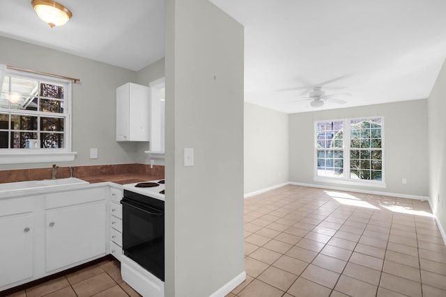 kitchen with light tile patterned flooring, range with electric stovetop, a sink, white cabinetry, and a ceiling fan