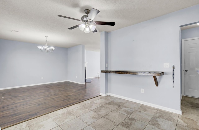 tiled spare room with ceiling fan with notable chandelier, a fireplace, and a textured ceiling