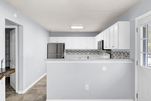 kitchen featuring kitchen peninsula, appliances with stainless steel finishes, backsplash, white cabinets, and light tile patterned flooring