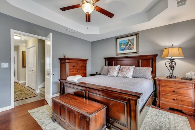 bedroom featuring wood-type flooring, a closet, a raised ceiling, and ceiling fan