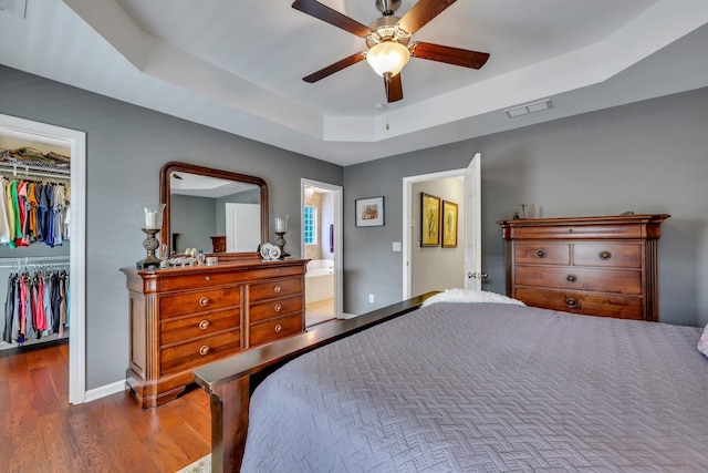 bedroom with ensuite bath, a raised ceiling, ceiling fan, dark hardwood / wood-style floors, and a closet