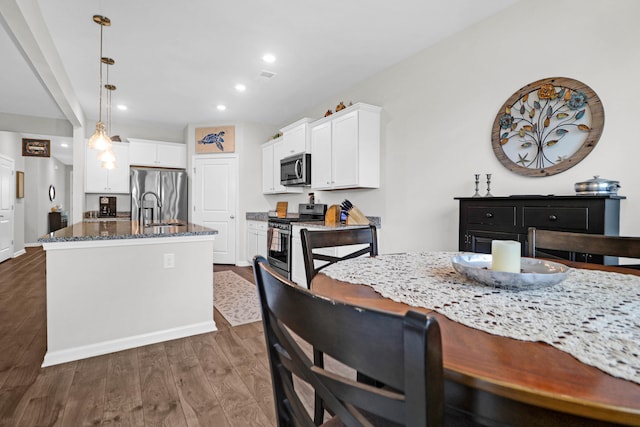 kitchen with stainless steel appliances, white cabinets, dark wood-type flooring, dark stone counters, and a center island with sink