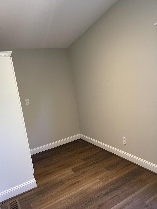 empty room with dark wood-type flooring, visible vents, and baseboards