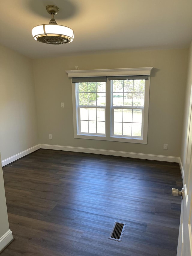 unfurnished room with dark wood-type flooring, visible vents, and baseboards