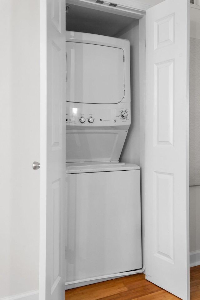 laundry area with stacked washer and dryer and wood-type flooring