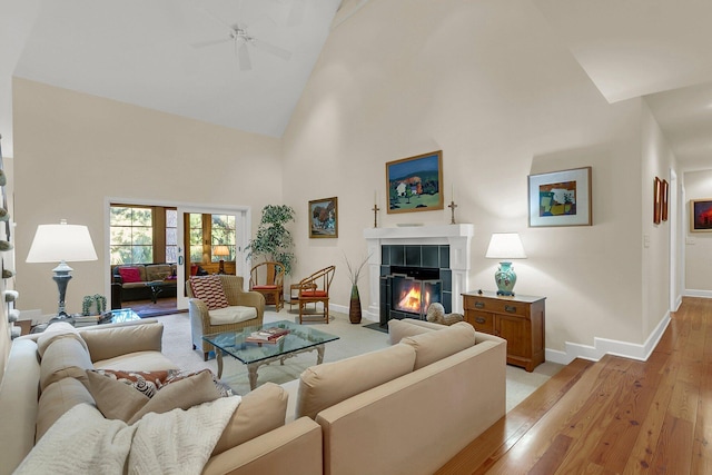 living room featuring ceiling fan, light hardwood / wood-style floors, high vaulted ceiling, and a tiled fireplace