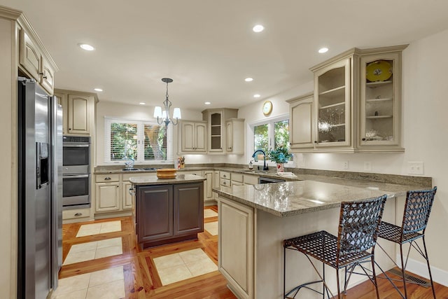 kitchen featuring kitchen peninsula, appliances with stainless steel finishes, sink, light tile patterned floors, and decorative light fixtures