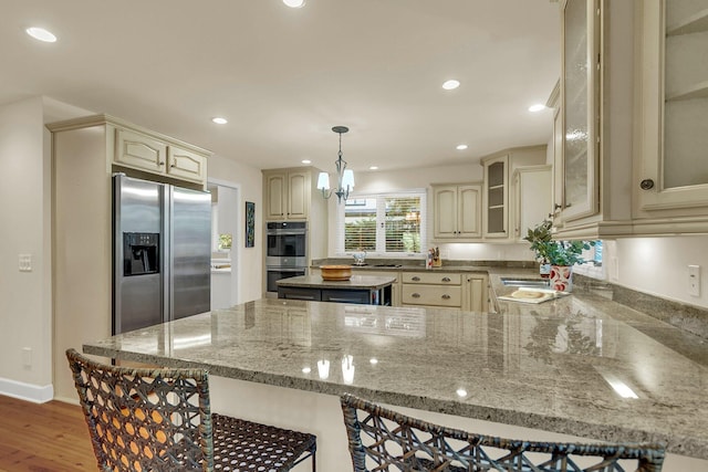 kitchen featuring a kitchen breakfast bar, light stone countertops, pendant lighting, and stainless steel appliances