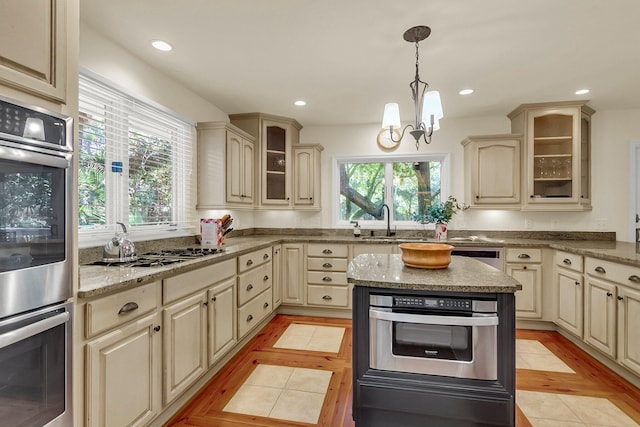 kitchen with cream cabinets, a chandelier, decorative light fixtures, light tile patterned floors, and appliances with stainless steel finishes