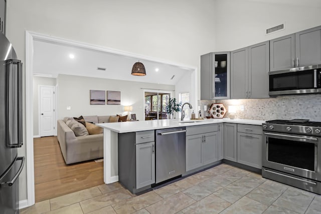 kitchen with kitchen peninsula, stainless steel appliances, gray cabinetry, and lofted ceiling