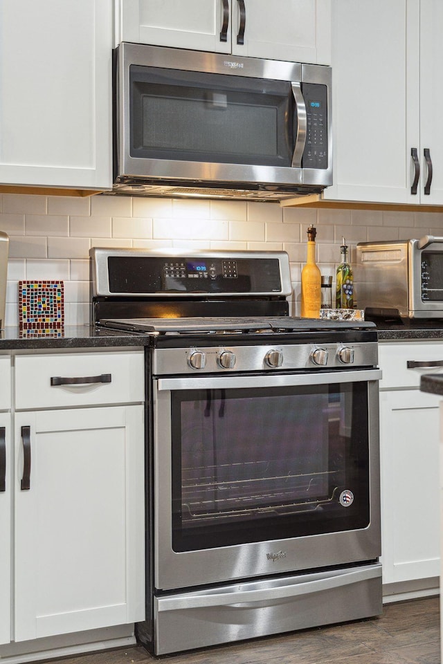 kitchen with tasteful backsplash, dark stone countertops, stainless steel appliances, wood finished floors, and white cabinetry