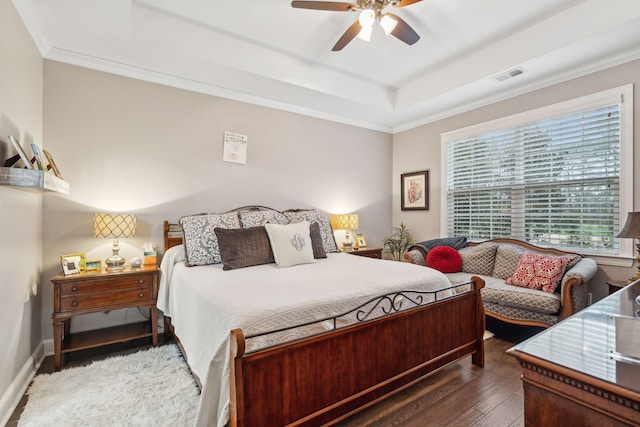 bedroom with baseboards, visible vents, a tray ceiling, ornamental molding, and hardwood / wood-style flooring