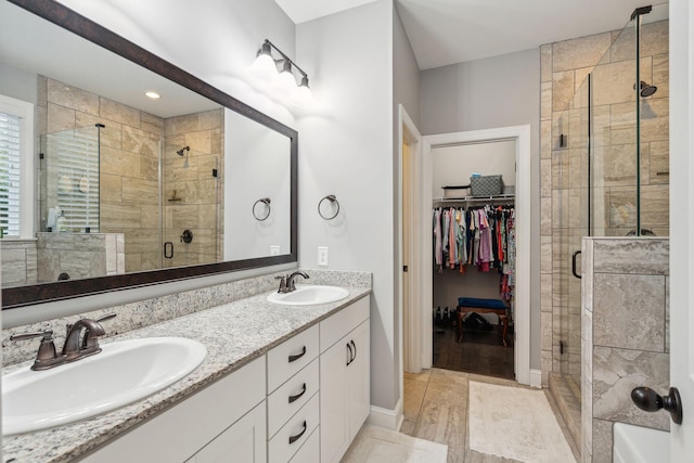 bathroom with a walk in closet, double vanity, a stall shower, and a sink