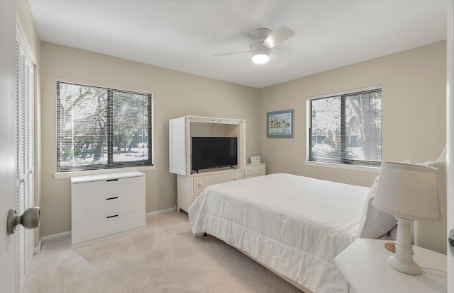 bedroom with baseboards, multiple windows, light carpet, and a ceiling fan