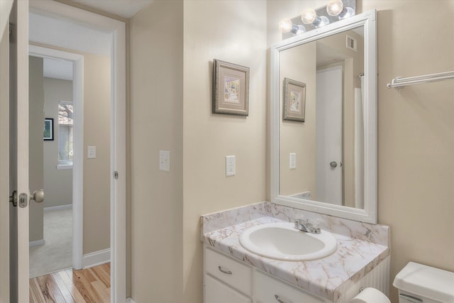 bathroom featuring visible vents, baseboards, toilet, wood finished floors, and vanity