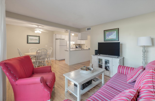 living room featuring light wood-style flooring, baseboards, visible vents, and ceiling fan