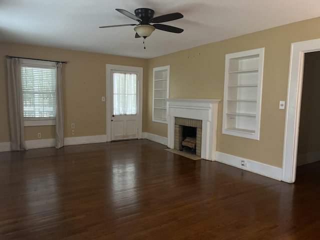 unfurnished living room with a brick fireplace, dark wood-type flooring, built in features, and ceiling fan