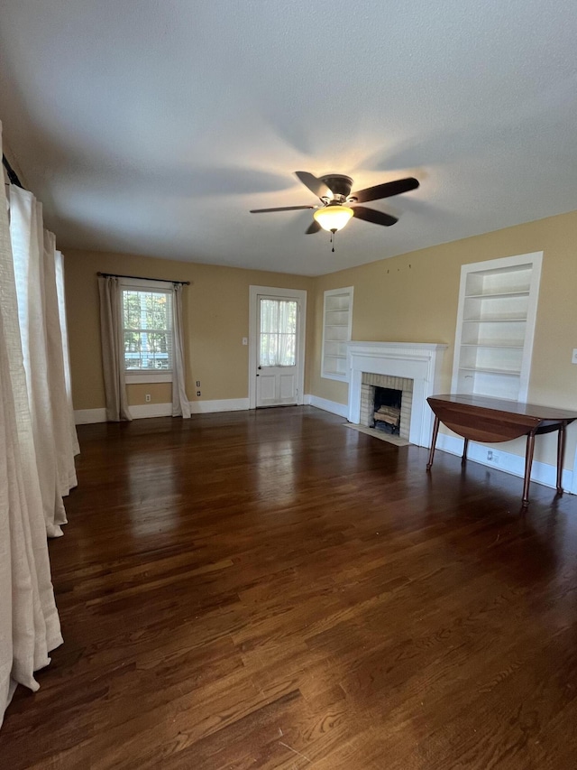 unfurnished living room featuring dark hardwood / wood-style floors, ceiling fan, a brick fireplace, a textured ceiling, and built in shelves