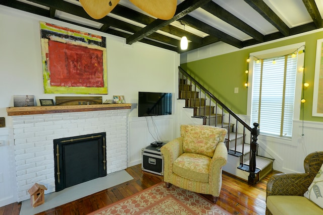 living room with beamed ceiling, wood-type flooring, and a brick fireplace