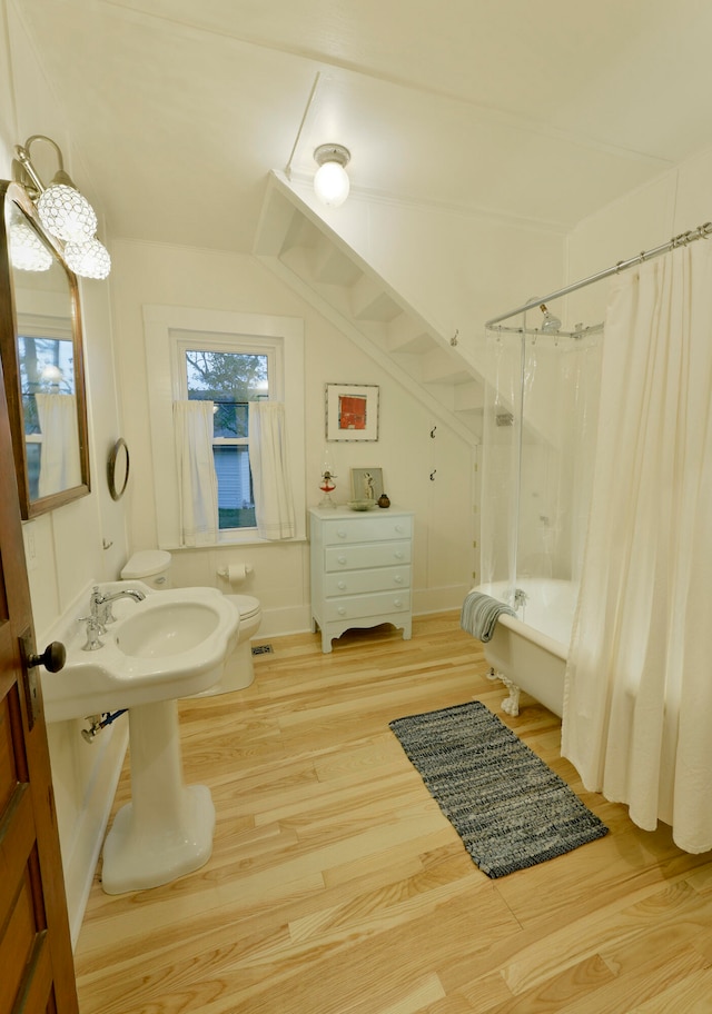 bathroom featuring toilet, wood-type flooring, shower / tub combo, and vaulted ceiling