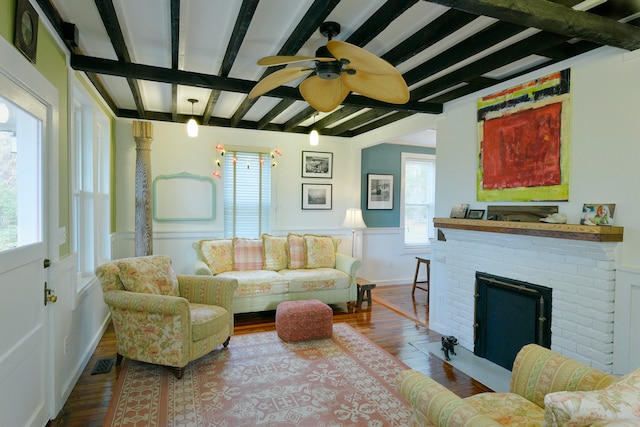 living room with beam ceiling, hardwood / wood-style floors, a brick fireplace, and a healthy amount of sunlight