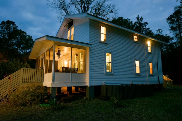 back house at dusk with a lawn and a sunroom