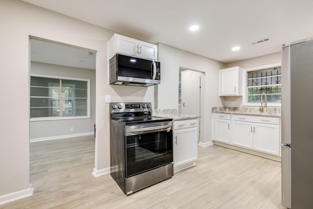 kitchen with white cabinetry, sink, stainless steel appliances, light stone counters, and light wood-type flooring