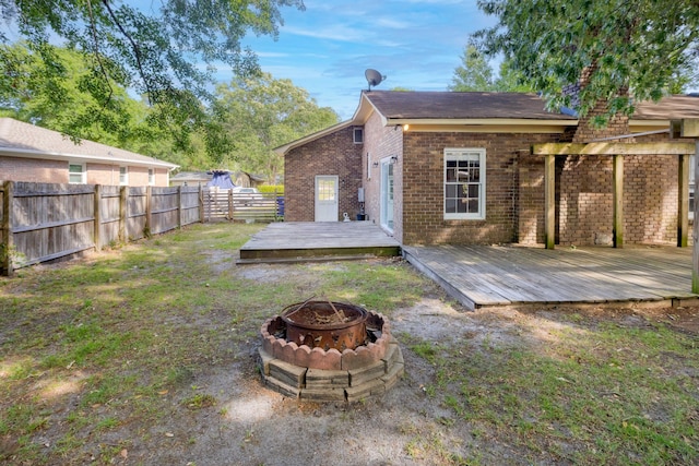 rear view of property with brick siding, a fenced backyard, an outdoor fire pit, and a wooden deck