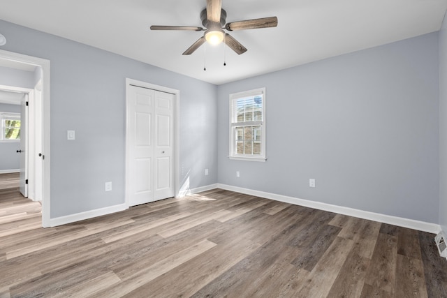 unfurnished bedroom with baseboards, multiple windows, a closet, and wood finished floors