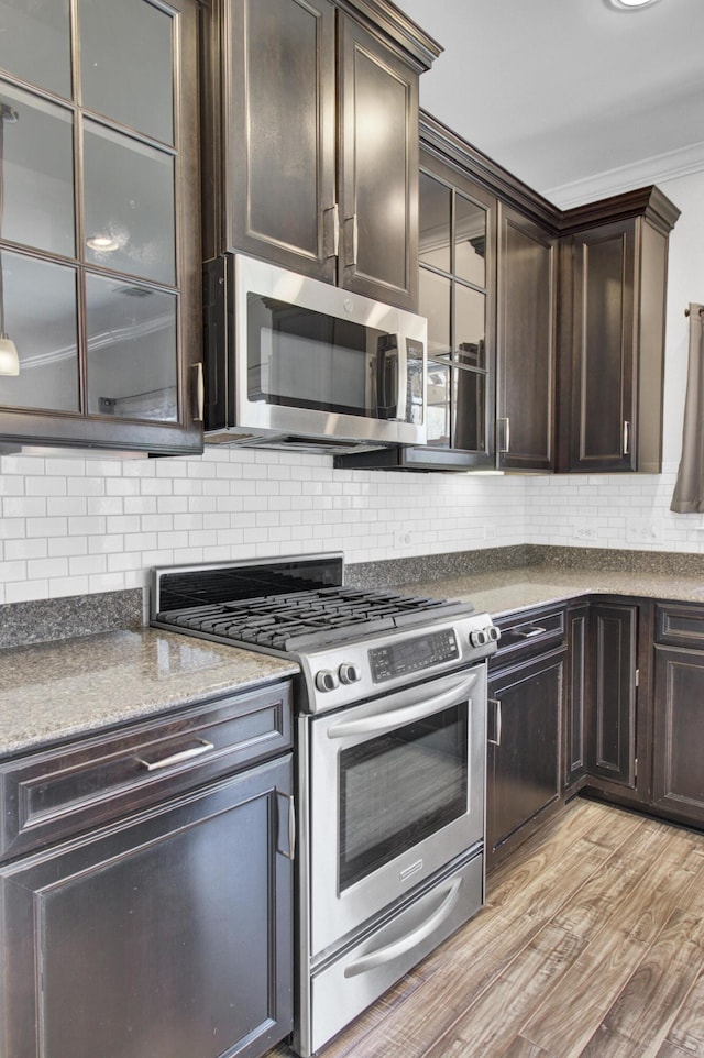 kitchen with stainless steel appliances, dark brown cabinets, crown molding, light wood-type flooring, and backsplash