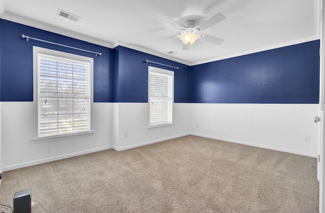 carpeted empty room with visible vents, wainscoting, and a ceiling fan