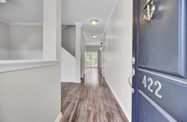 corridor with dark wood-style floors, a wainscoted wall, crown molding, and baseboards