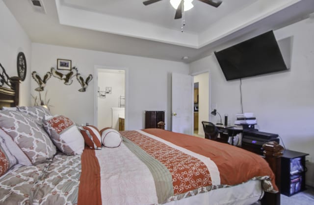 bedroom with ceiling fan, a raised ceiling, and ensuite bath