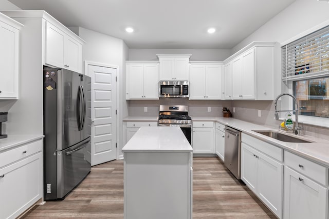 kitchen featuring appliances with stainless steel finishes, light wood-type flooring, a center island, white cabinets, and sink