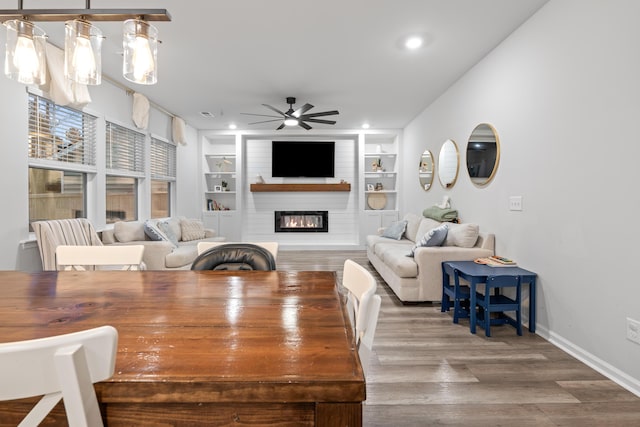 living room featuring ceiling fan, wood-type flooring, built in shelves, and a fireplace