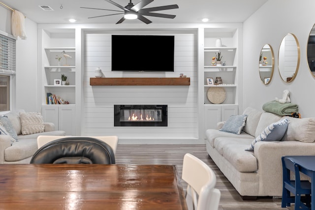 living room featuring a large fireplace, ceiling fan, dark hardwood / wood-style flooring, and built in shelves