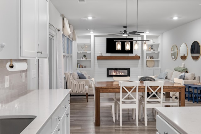 kitchen featuring decorative light fixtures, white cabinetry, a fireplace, light stone countertops, and dark wood-type flooring