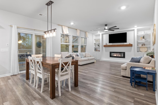 dining room with a large fireplace, ceiling fan, plenty of natural light, and built in shelves