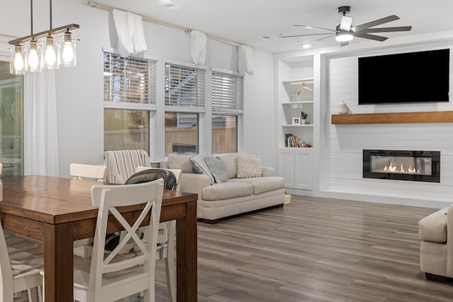 living room with a large fireplace, hardwood / wood-style flooring, built in features, and ceiling fan