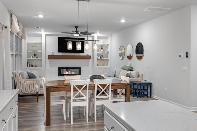 dining area with ceiling fan, dark wood-type flooring, built in features, and a fireplace