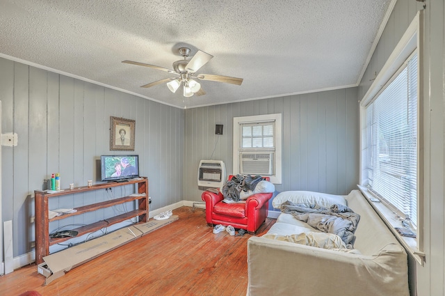 sitting room with crown molding, ceiling fan, heating unit, wood-type flooring, and a textured ceiling