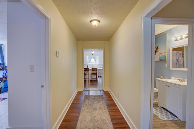 hallway with baseboards, a sink, a textured ceiling, and wood finished floors