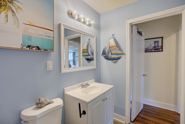 half bathroom with vanity, baseboards, wood finished floors, and toilet
