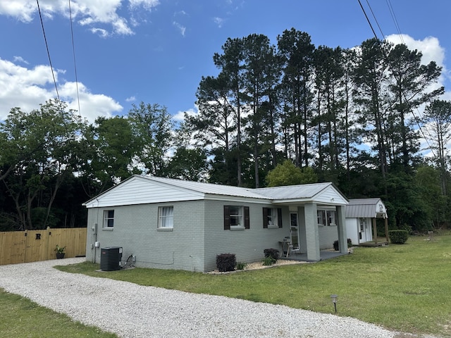 exterior space featuring metal roof, central air condition unit, brick siding, fence, and a yard