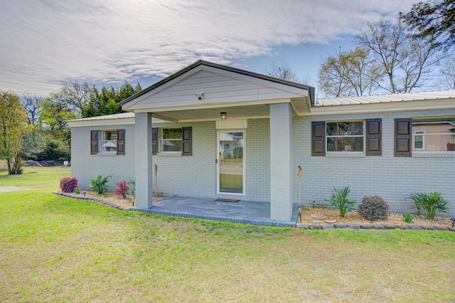 ranch-style home with brick siding, a patio area, a front yard, and metal roof