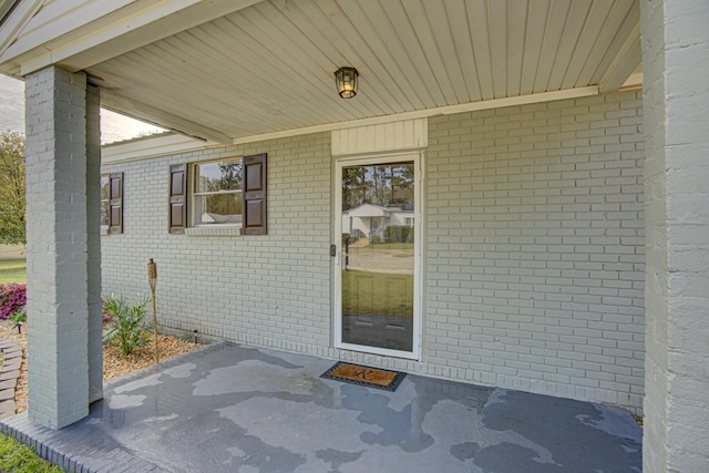 view of exterior entry featuring brick siding and a patio area
