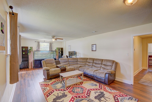 living area featuring visible vents, wood finished floors, baseboards, a textured ceiling, and a ceiling fan